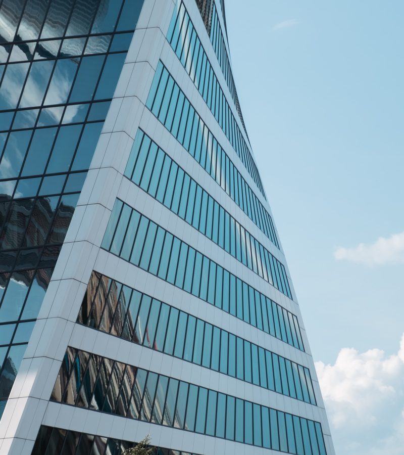 View of glass facade of skyscraper and blue sky with white clouds. Modern architecture, urban space. Abstract background.